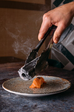 Chef toasting a salmon nigiri with a piece of charcoal