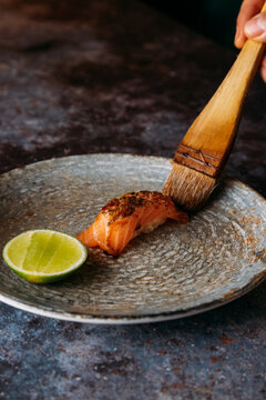Chef painting a salmon nigiri with soy sauce using a wide brush