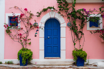 Fototapeta na wymiar Traditional greek house with colorful blue door and pink walls at Asos village. Assos peninsula famous and extremely popular travel destination in Cephalonia, Greece, Europe.
