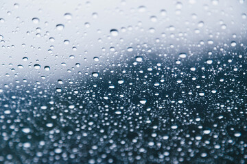 Naklejka na ściany i meble Close up of rain drops on the windshield, front window of a car on a blue gray background of dark sky.