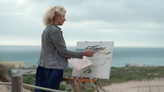 Middle-aged European woman, artist, paints a seascape with an original view of the sea. Slow motion