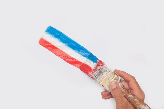 Hand holding paintbrush with stripe of red white and blue paint