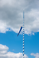 bavarian flag, hoisted on a maypole, against blue sky with clouds