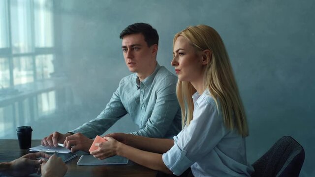 Tracking shot of serious professional young woman and man headhunters holding interview with male job seeker sitting at desk. Job interview - female head hunter asking questions during interview.