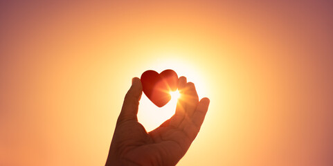 Plakat The magic of love symbol. Hand holding heart up to the sun. 