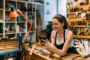 Woman Luthier using a smartphone in guitar workshop