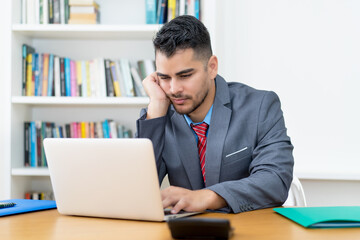 Mexican businessman watching boring video call at computer