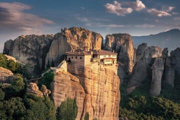 Fototapeta na wymiar Scenic aerial view of a brightly lit Christian monastery on top of a bizarre cliff surrounded by mountain cliffs at sunset, Meteora, Greece