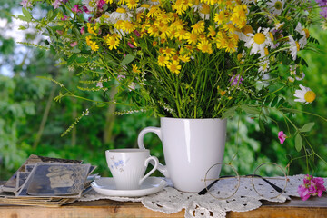 female hands going through old photos of 40s, 50s, bouquet of wildflowers, handmade lacy, cup of tea on table in garden, concept of genealogy, memory of ancestors, family tree, family archive
