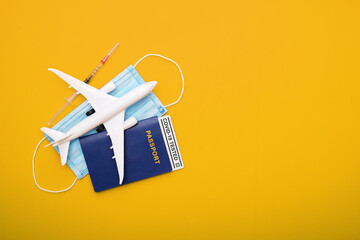 Syringe, toy plane, medical mask and passport with Covid-19 test  with text 'Covid-19 tested' inside it on yellow background. Travel concept during the Covid-19 pandemic