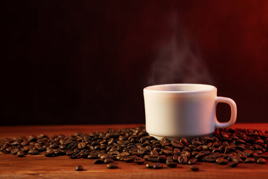 Warm cup of coffee and coffee beans on dark background. Coffee cup and coffee beans on wooden table © spyrakot