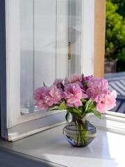 Vertical photo. Bouquet of bright pink peonies in a vase in an open window. French mood