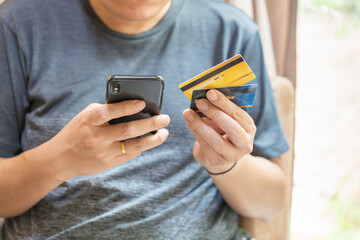 Business, Financial, Payment and Technology Concept. Asian man holding two FAKE mockup credit card and using mobile smartphone.