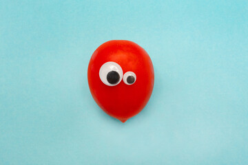 Red tomato with googly eyes. A funny face. Round eyes. Blue background. Holiday.