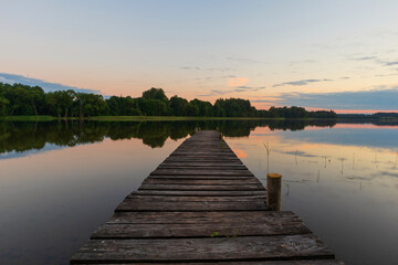 View of the lake with a wooden footbridge in the center of the photo. Outdoor summer evening