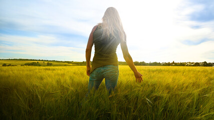 	Woman in jeans and t-shirt relaxe in nature wheat or barley cornfield at sunset - holds hand to ears of corn	