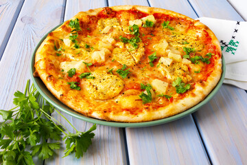 Pizza with with pineapple, chicken and mozzarella on white wooden table.