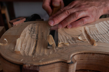 Luthier's hands using gouge to work the wood and make a violin