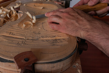 Luthier's hands using gouge to work the wood and make a violin