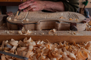 Luthier's hands using gouge to work the wood and make a violin