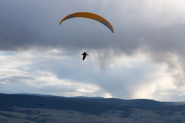 Adventurous People Flying on a Paraglider around the mountains. Savona, British Columbia, Canada.