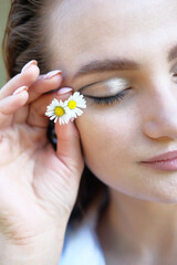 Portrait of a girl with closed eyes. Daisies in the hand near the face 