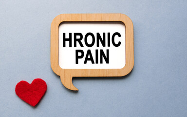 The inscription HRONIC PAIN on a wooden template, against the background of scattered a red heart. Medical concept.
