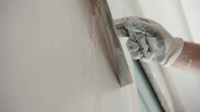 Close-up of reconstructed wall on construction site in new buyed apartment, building master puttying and aligning wall with metal spatula and finishing spackling paste solution. Process of