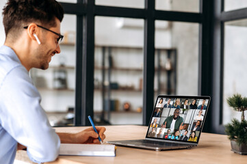 Successful caucasian male manager, takes notes during online business meeting with multinational...