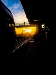 Silhouette d'un homme sur un pont observant un train &agrave; l'arr&ecirc;t &agrave; une gare, face au couch&eacute; du soleil 