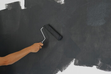 Close-up of a male hand painting a wall in black.