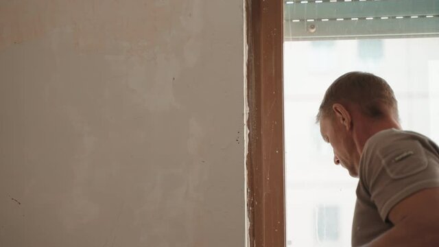 Building worker using professional tools for plasterworks on construction site, repairman aligning and smoothing wall surface with metal spatula and spackling paste. Engineering industry