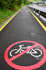 Obraz premium In the foreground, below, on an asphalt footpath, there is a prohibiting cyclist sign. In the background, in perspective, a leaving empty jogging track