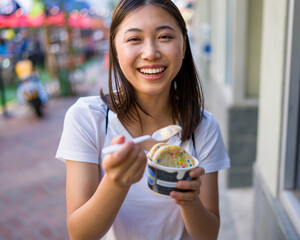 Happy Young Asian Woman Wearing Distressed Jeans and T-Shirt Eating an Ice Cream Sandwich in a Downtown Urban Area