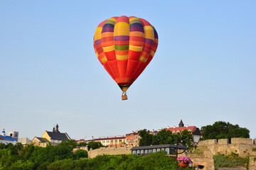 Fototapeta na wymiar A large multicolored hot air balloon flies low over ancient buildings and a tree-lined valley. Photographed at close range