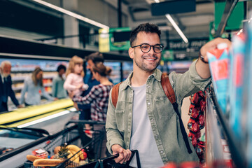 Young man buying groceries at the supermarket. Other customers in background. Consumerism concept.