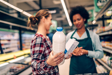 Young woman buying groceries at the supermarket. Other customers in background. Consumerism concept.