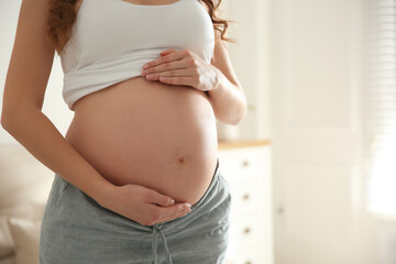 Pregnant woman touching her belly indoors, closeup - obrazy, fototapety, plakaty