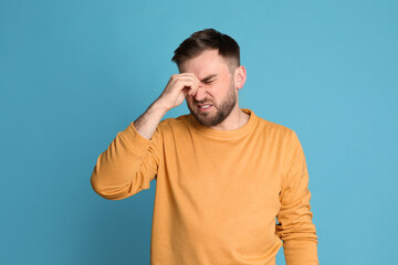 Man suffering from migraine on light blue background