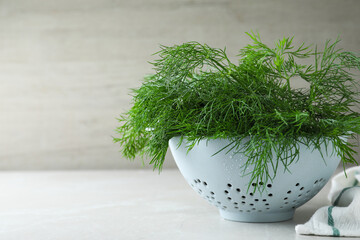 Fresh dill in colander on white table, space for text