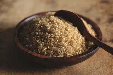 Brown sugar in a wooden dish set against an old wooden background.