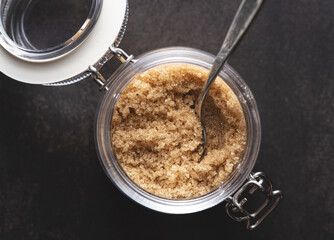 Brown sugar and a spoon in a glass container set against a black stone background.