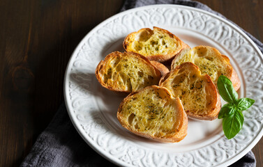 Sliced baked bread with garlic and herbs on a white plate on the table.