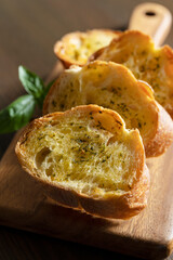 Sliced baked bread with garlic and herbs on a wooden cutting board on the table.