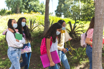A group of Latina adolescent women with a mask as a prevention of covid 19 walk down the street towards high school