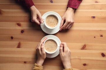 Women with cups of coffee at wooden table, top view