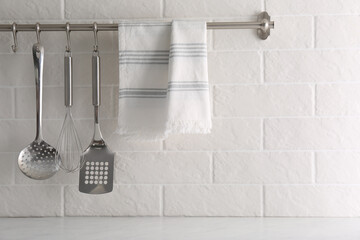 Soft kitchen towel and utensils hanging on rack near white brick wall