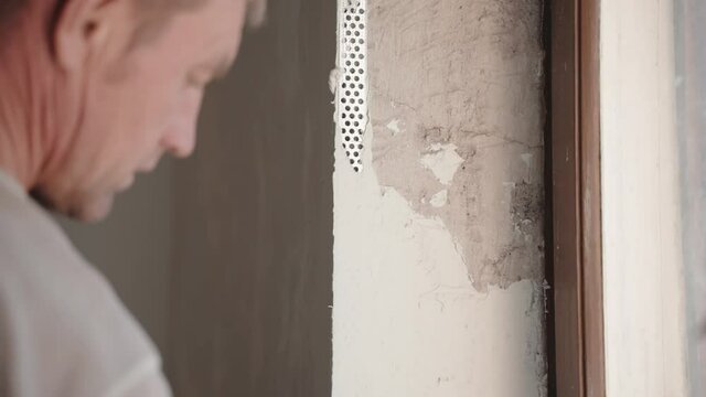 Repairman working hard on construction site, male builder puttying walls and angles with spackling paste using metal spatula. Repairing works and walls reconstruction