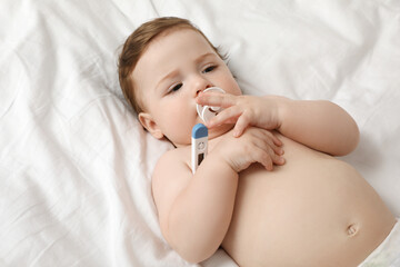 Adorable baby with thermometer on bed. Measuring temperature