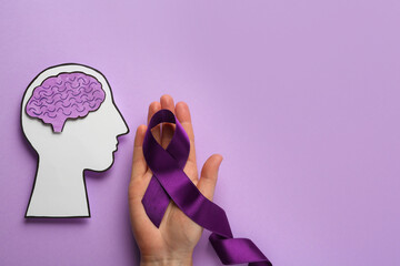 Woman holding purple ribbon near paper human head cutout over violet background, top view. Epilepsy...